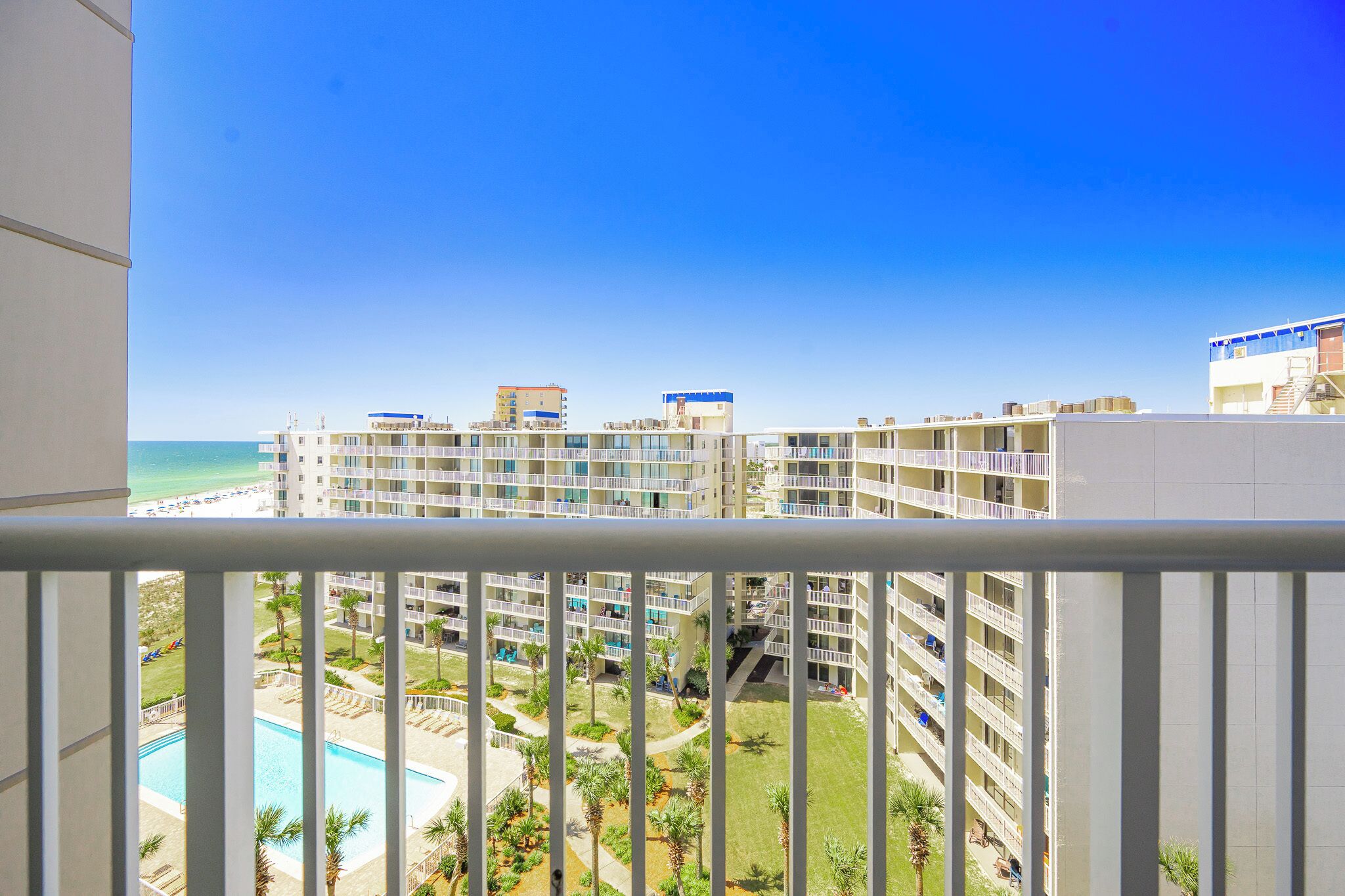 A high-rise hotel with multiple balconies, a swimming pool, and a view of the beach.