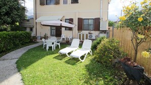 A two-story building with a patio area featuring white chairs and a table under a canopy.