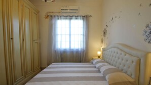 A bedroom with a large bed, a nightstand, a wardrobe, a window with curtains, and wall decorations.