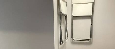 A corner of a room with a white radiator, a black appliance, and a white wall-mounted shelf.
