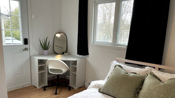 Quarto com cama, escrivaninha com cadeira, planta em vaso e janela com cortinas.