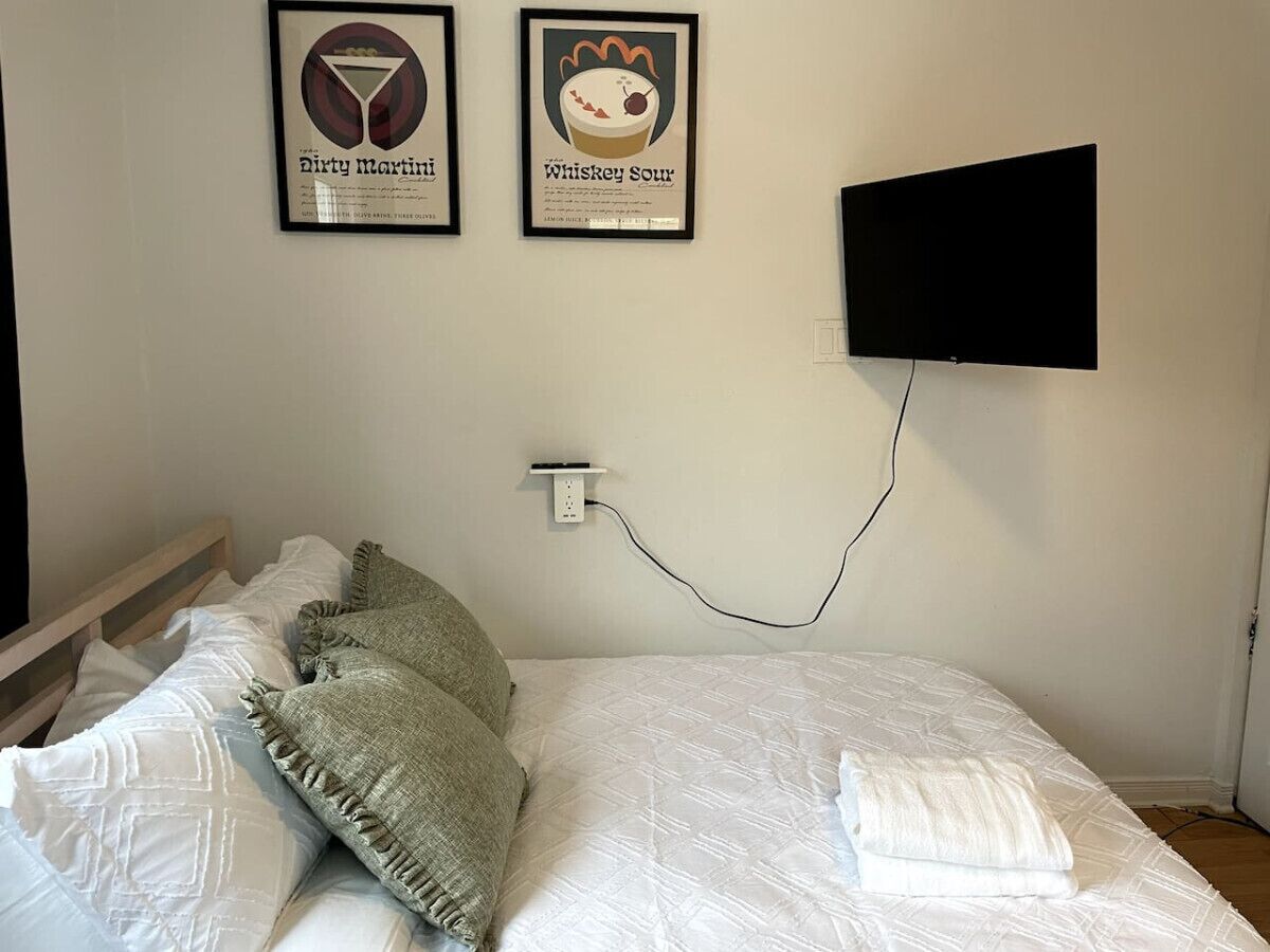 Une chambre à coucher avec un lit, des oreillers, un téléviseur fixé au mur et deux tableaux encadrés.