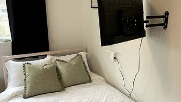 A neatly made bed with white bedding and two pillows, a black curtain on the window, and two framed pictures on the wall.
