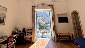 Une chambre d’hôtel avec un plancher en bois, un lit, un bureau avec une chaise, une télévision et un balcon offrant une vue sur un paysage montagneux.