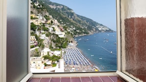 Une ville côtière avec des bâtiments construits sur une colline, une plage parsemée de parasols et des bateaux sur l’eau.