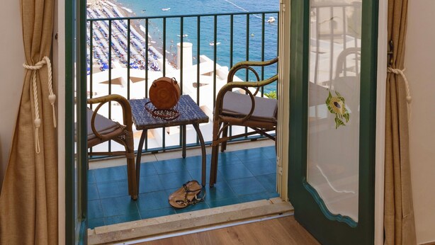 Un balcon avec vue sur la mer, une chaise, une table et un sac suspendu.