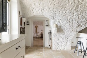 A room with a rustic stone wall, a wooden door leading to another room, a white dresser, and a bar area with stools. - Terrazza Olivia Maria by Wonderful Italy (Ostuni)
