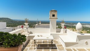 Una terraza en la azotea con una mesa, plantas en macetas y vistas a la costa.