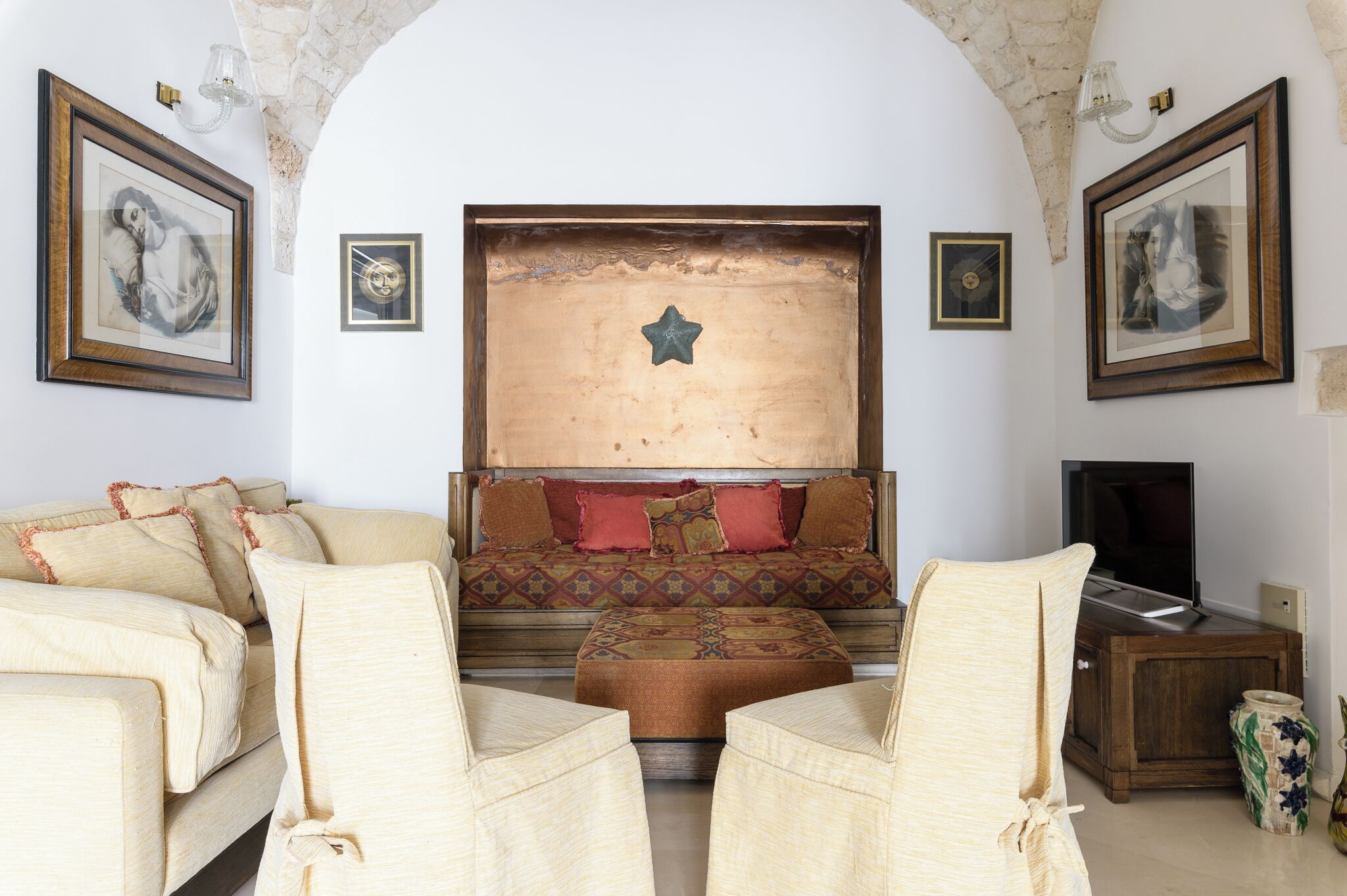 A cozy living room with a sofa, two armchairs, a television, and framed artwork on the walls.
