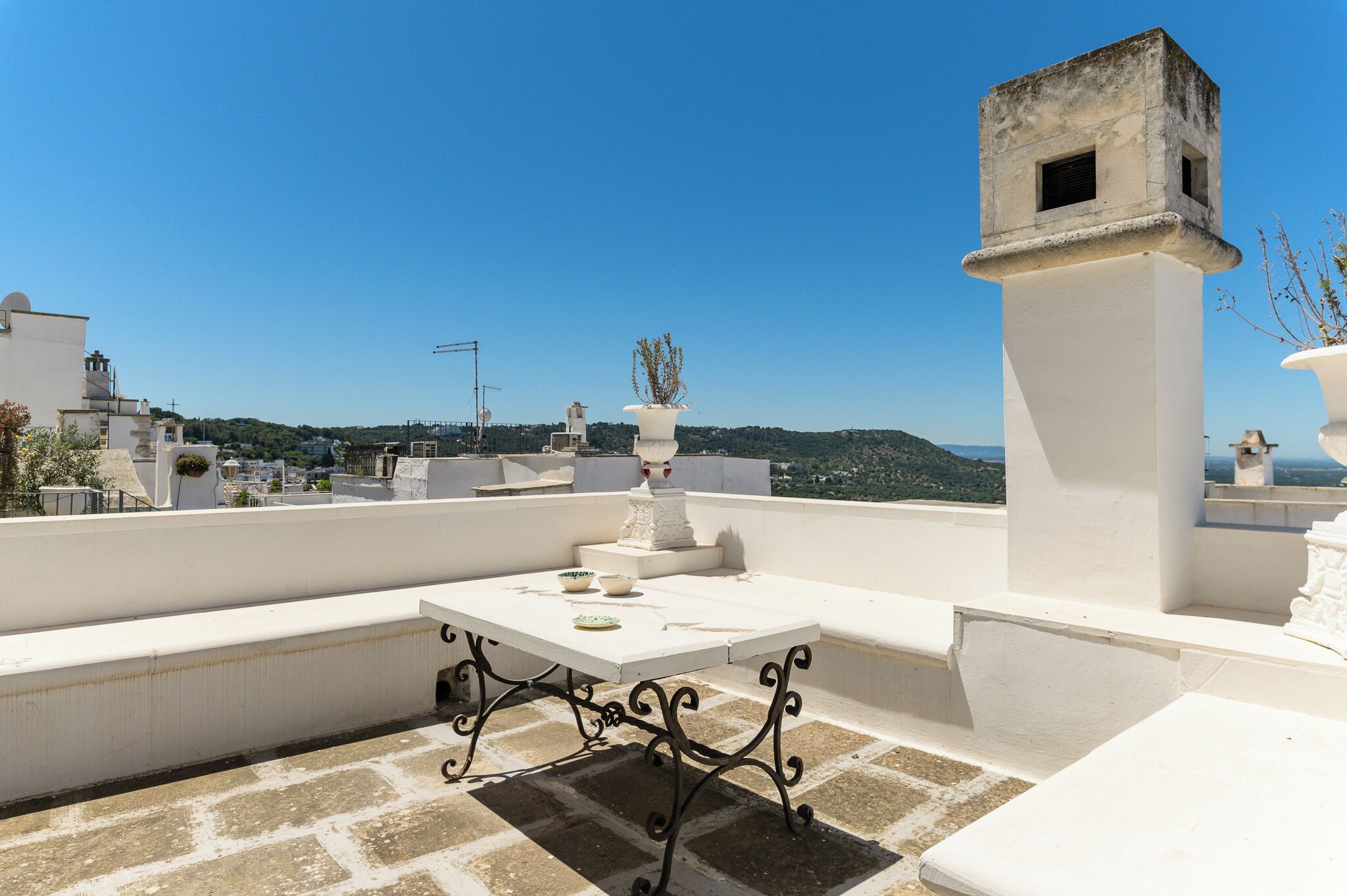 Une terrasse sur le toit avec une table et des chaises blanches, un vase décoratif et une vue sur le paysage urbain.