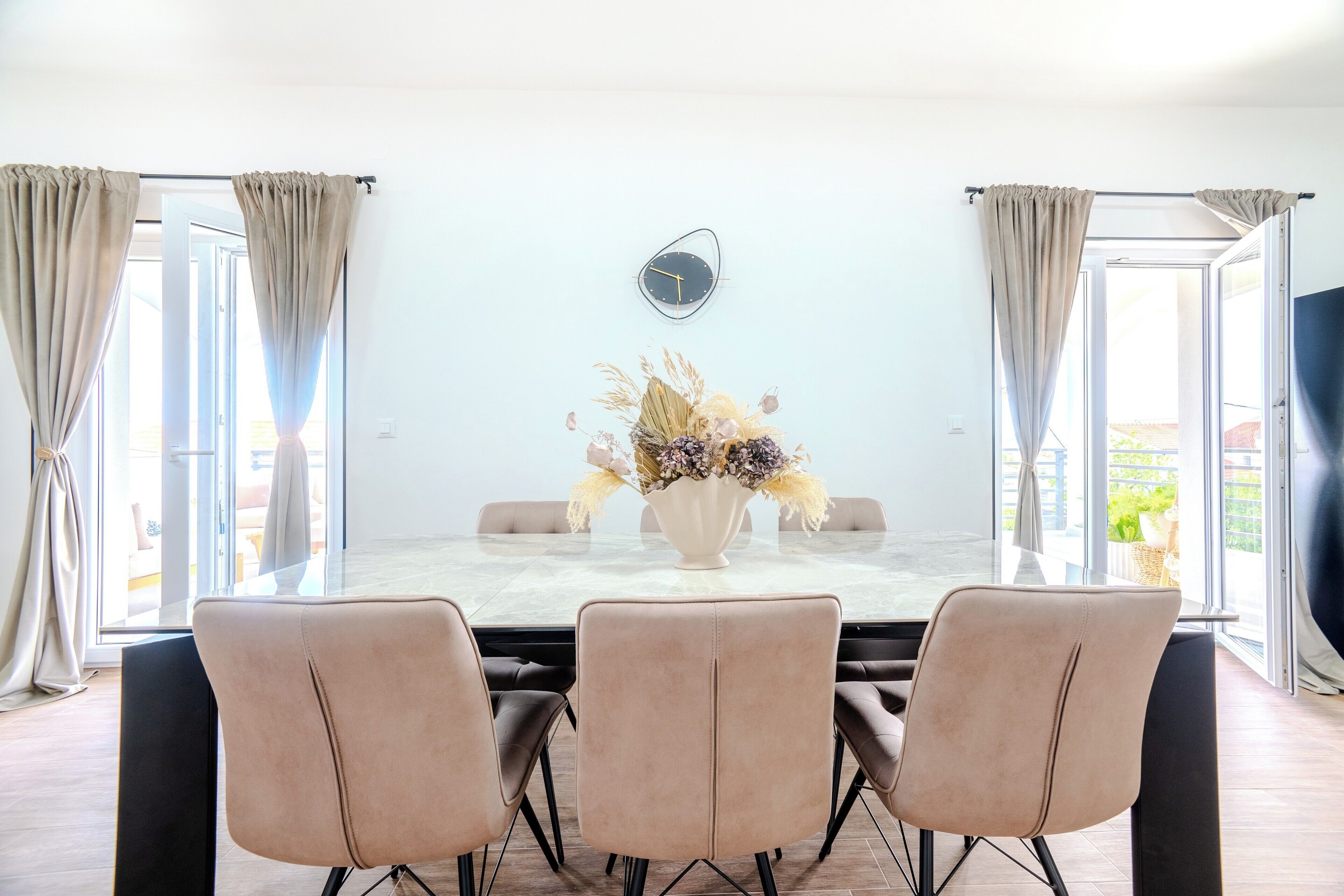A dining area with a marble table, beige chairs, and a vase of flowers.