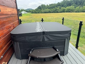 A hot tub on a wooden deck with a view of a grassy field and trees in the background.