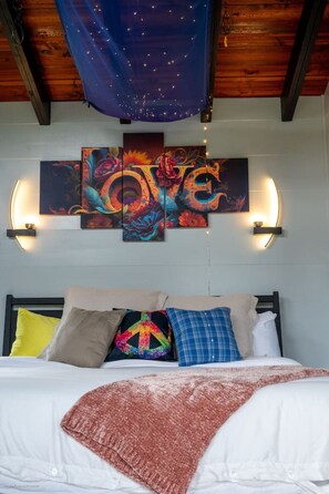 A bedroom with a bed, colorful artwork, and wall-mounted lights.