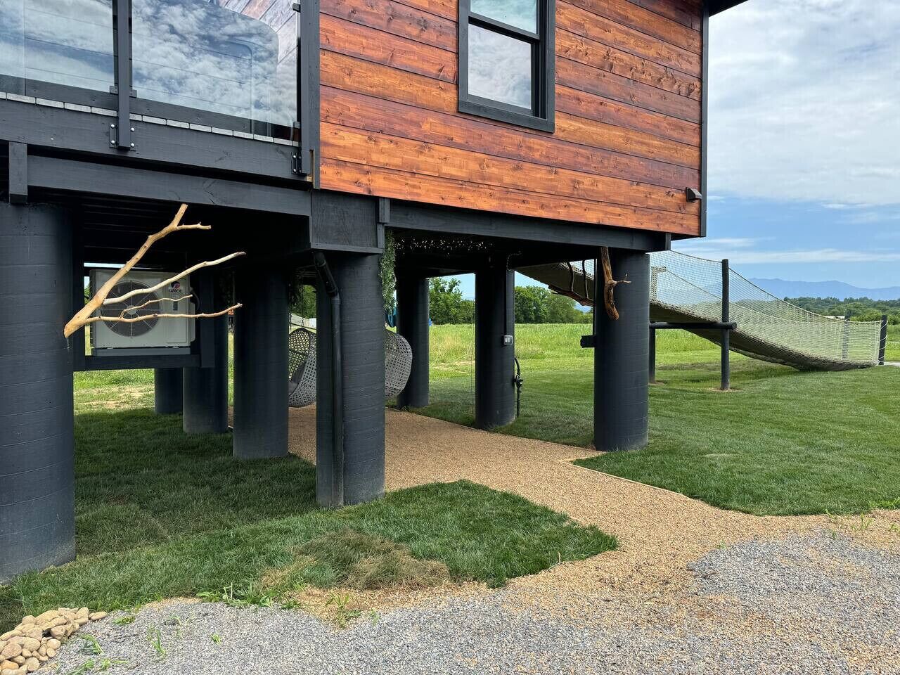Een modern huis met een houten gevel en zwarte pilaren, een grindpad en een gazon met een hangmat.