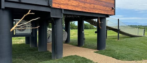 Ein modernes Haus mit Holzfassade und schwarzen Säulen, einer Schotterauffahrt und einer Rasenfläche mit einer Hängematte.
