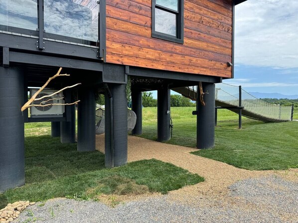 A modern house with a wooden exterior and black pillars, a gravel driveway, and a grassy area with a hammock.
