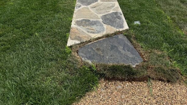 A stone pathway leading to a fenced area with a view of distant mountains.