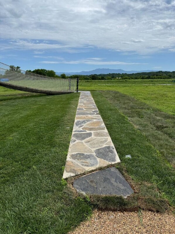 A stone pathway leading to a fenced area with a view of distant mountains.