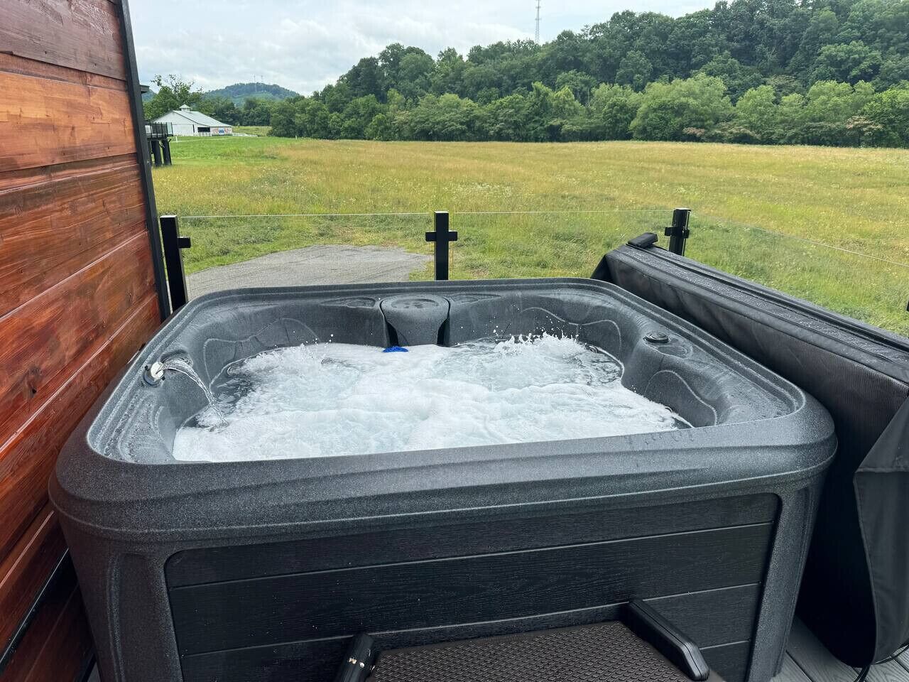 A hot tub with a wooden exterior wall and a view of a grassy field and trees in the background.
