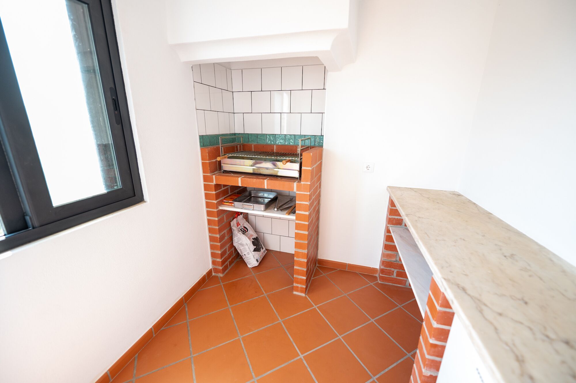 Una cocina compacta con salpicadero de ladrillo, una parrilla empotrada y un ventanal.