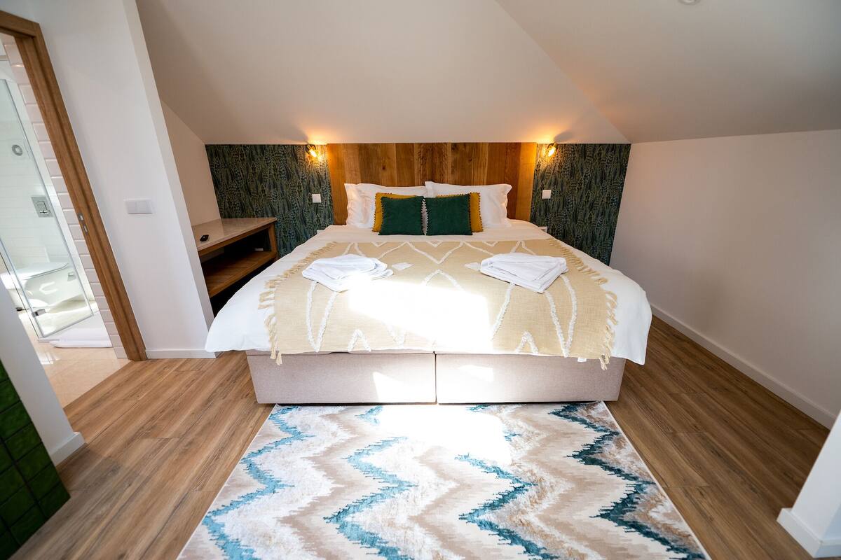 A neatly arranged bedroom with a bed, a small seating area, and a patterned rug.