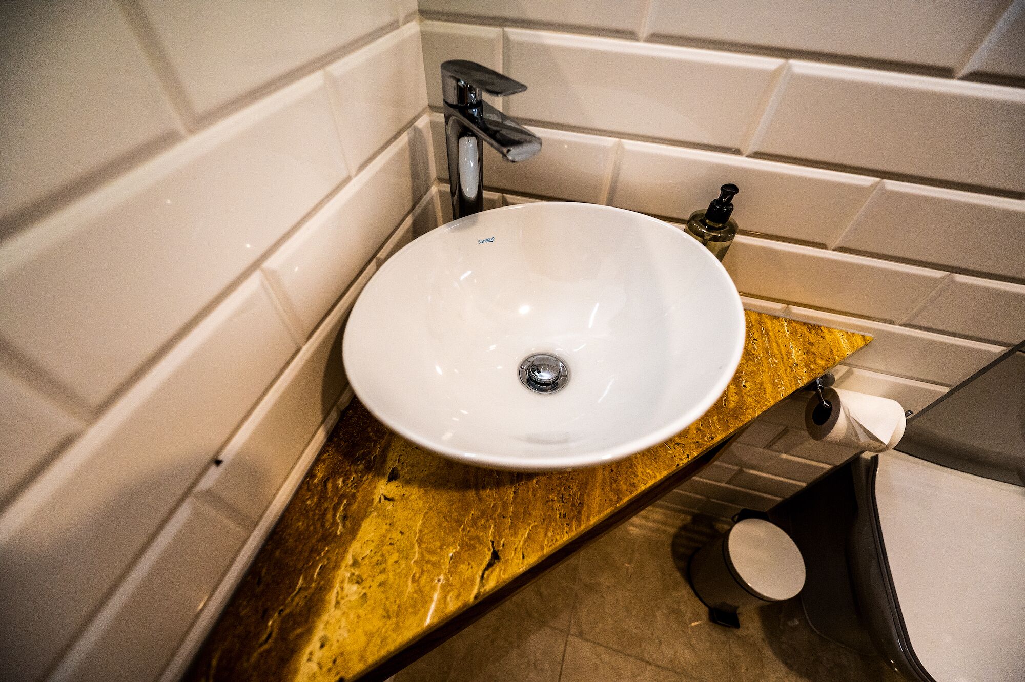 Een badkamer met een witte wastafel, een goudkleurig aanrecht en een zwart toilet.