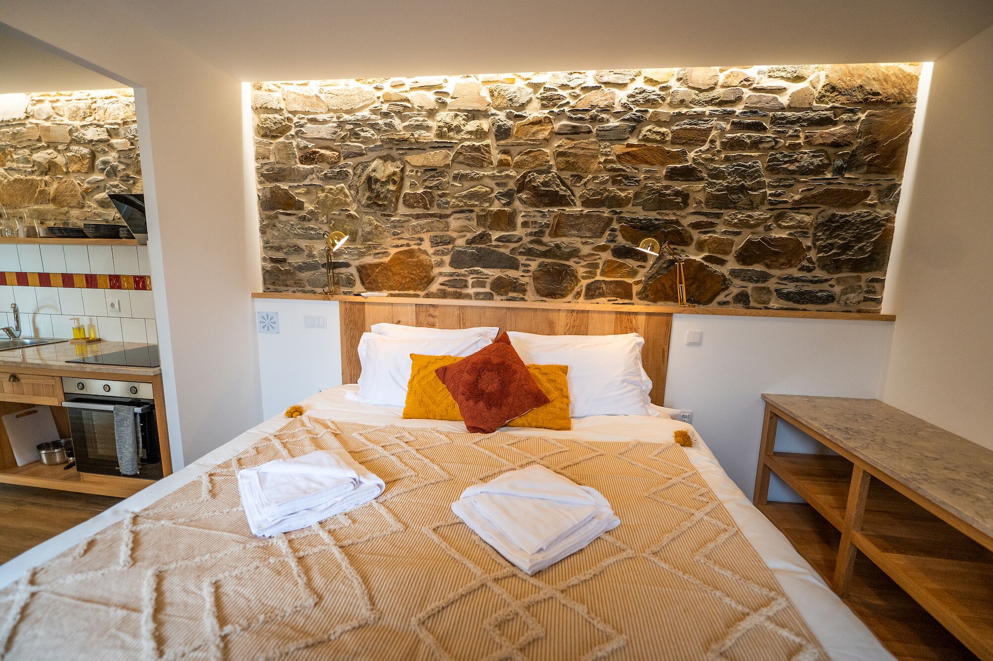 Ein Schlafzimmer mit Steinswand, Holz-Kopfteil und einem Bett mit weißen und gelben Kissen.