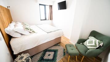 A bedroom with a bed, a green armchair, a TV, and a window.