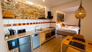 Une cuisine compacte avec un mur en pierre, un coin repas avec une table et des chaises, et un lit doté d’une tête de lit à motifs.