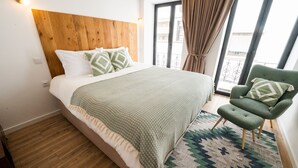 Une chambre à coucher avec une tête de lit en bois, une couvre-lit verte à motifs, un fauteuil vert et un tapis à motifs.