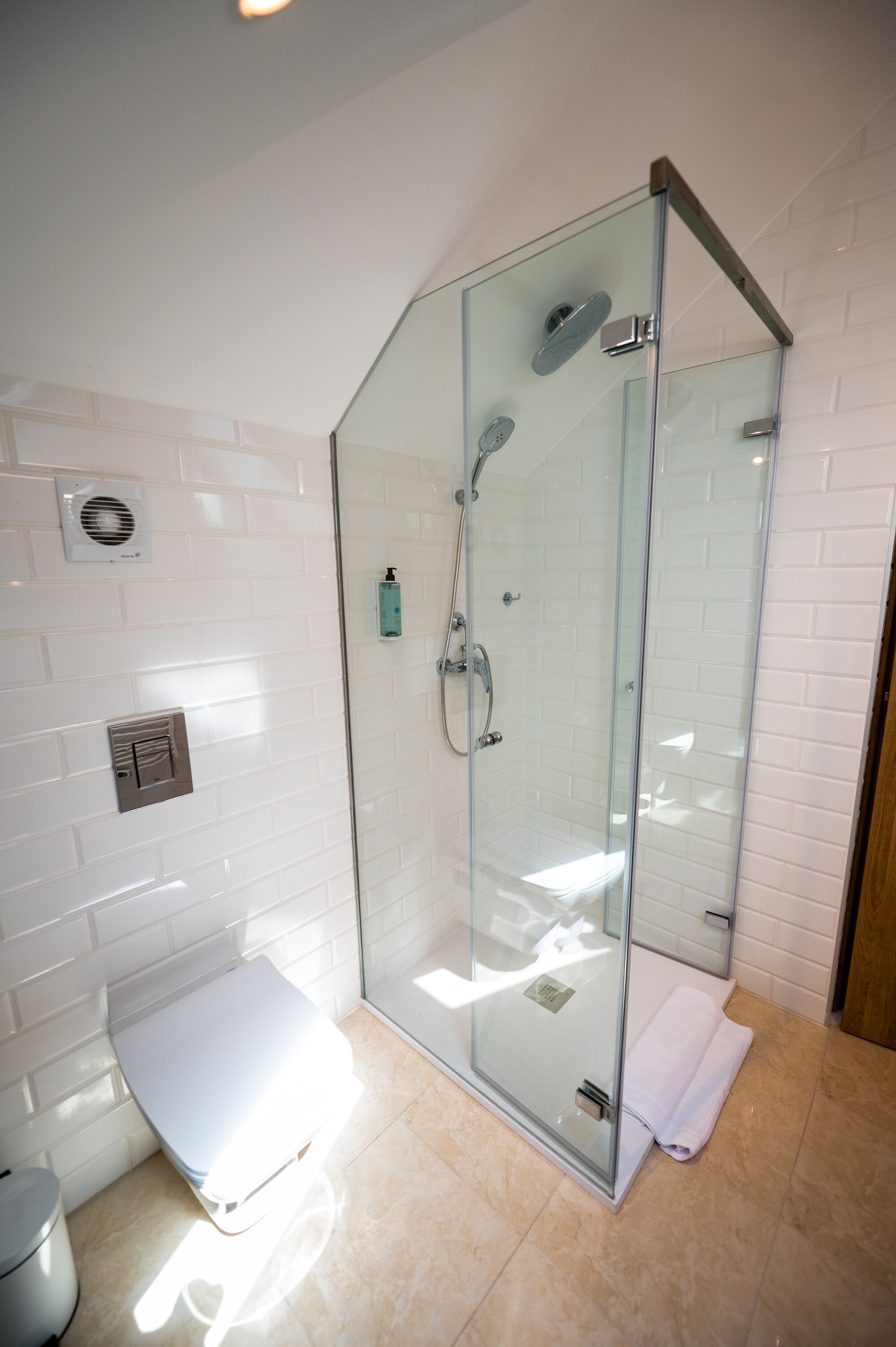 Un baño moderno con ducha acristalada, paredes de azulejos blancos y un inodoro blanco.