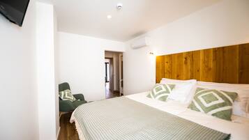 A bedroom with a wooden headboard, a bed with patterned bedding, a green armchair, and a television mounted on the wall.