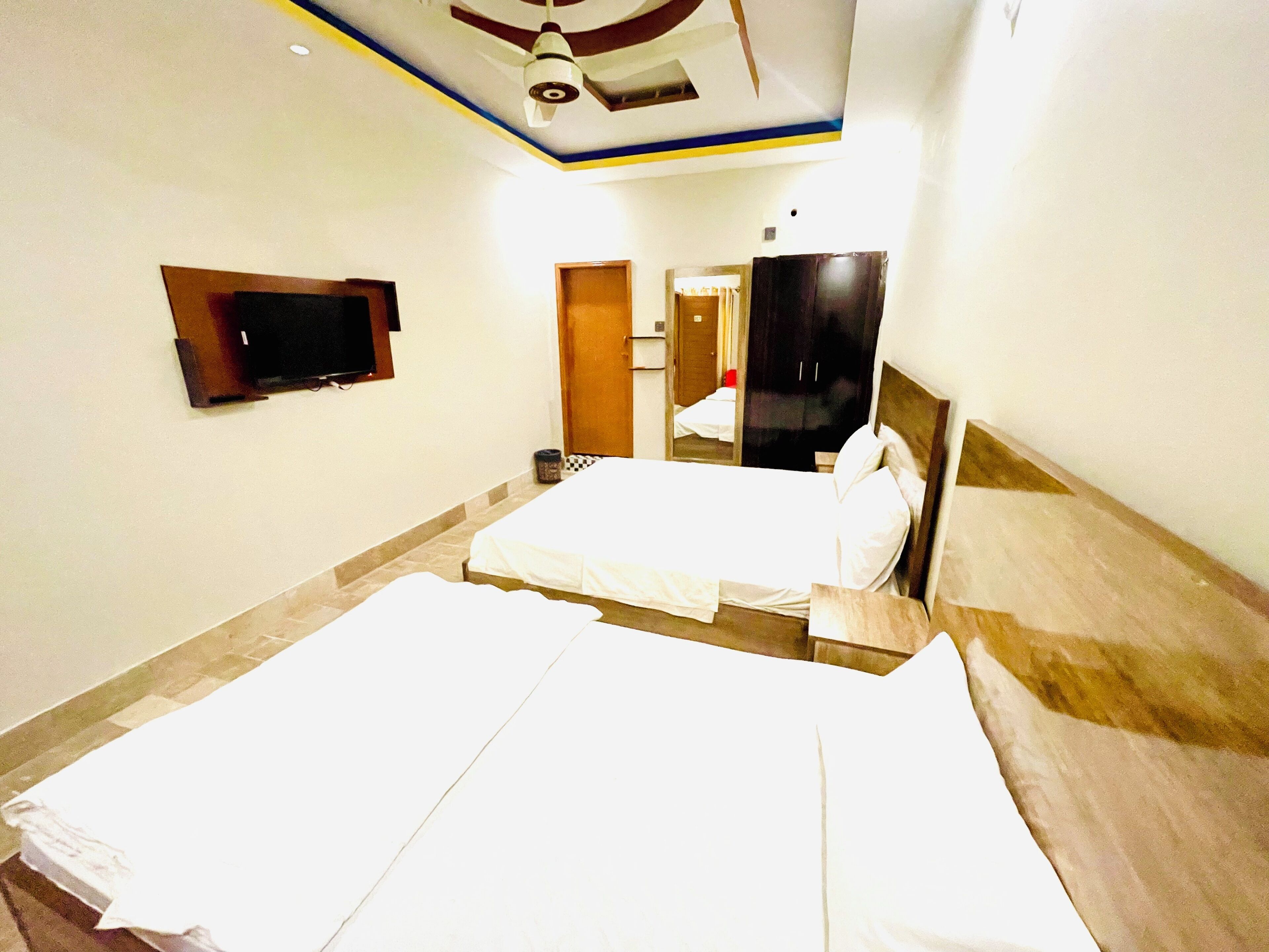 A hotel room with two beds, a TV mounted on the wall, and a ceiling fan.