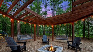 An outdoor seating area with Adirondack chairs, a stone fire pit, and a wooden pergola. - Pet Friendly Woodland Escape with Play Area (Broken Bow)
