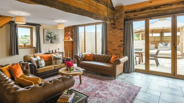 Un salon spacieux, doté de canapés en cuir, d’une table basse et d’une grande porte-fenêtre coulissante donnant sur une terrasse extérieure.