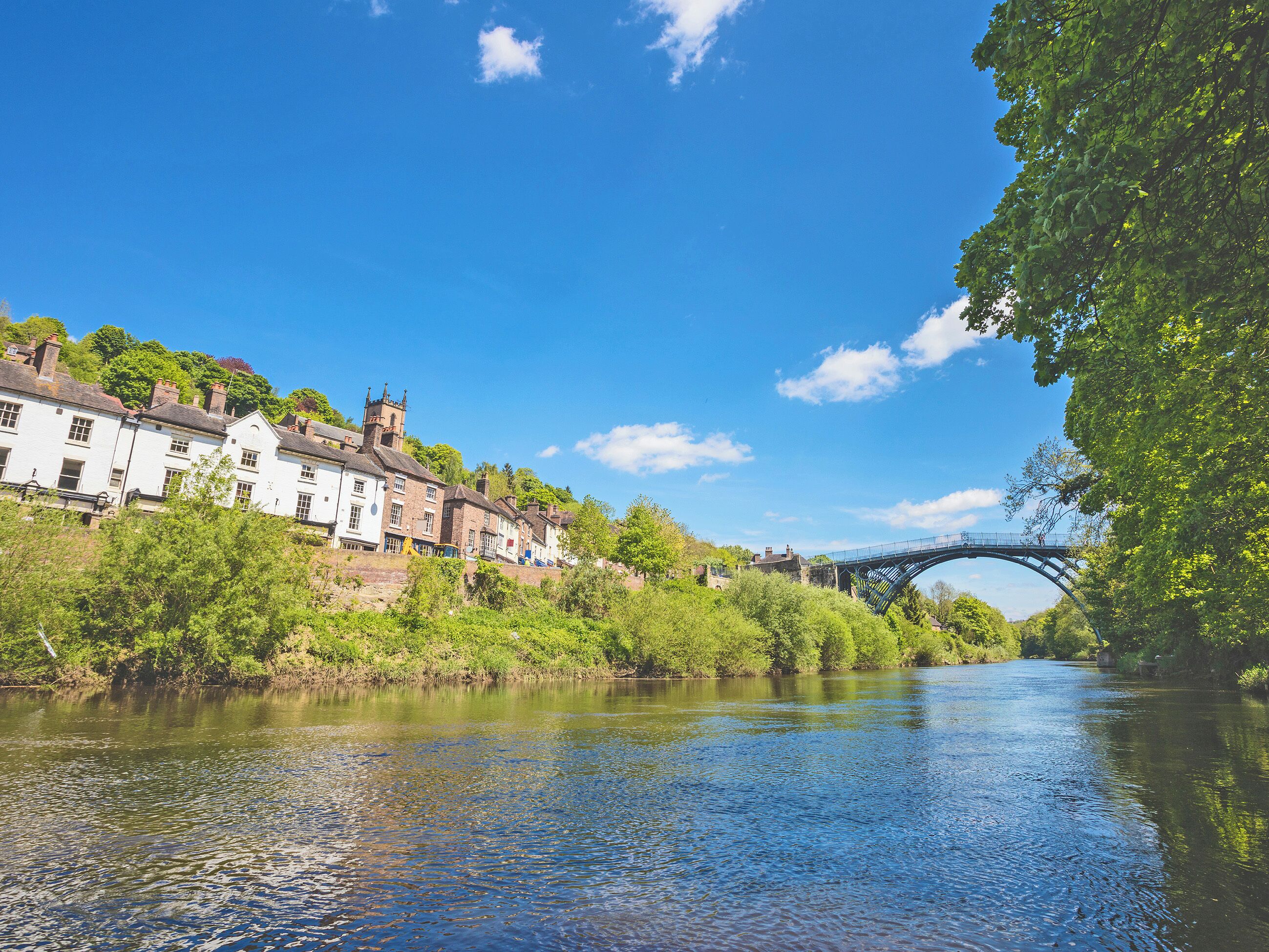A river with a bridge, buildings on the riverbank, and greenery.