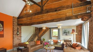 Un vaste salon doté d’un haut plafond en bois, d’un escalier et d’une grande fenêtre agrémentée de rideaux.