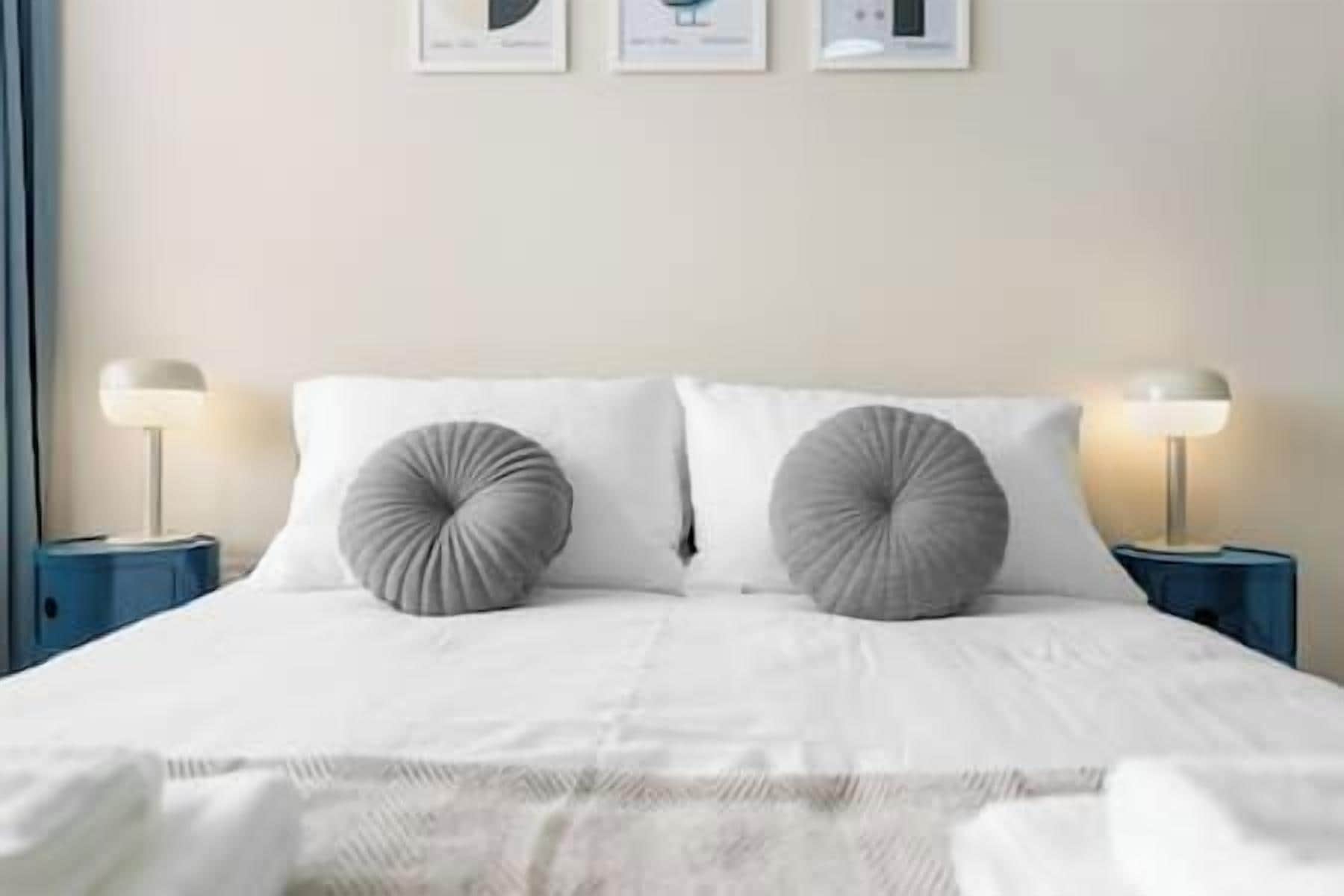A bed with two round pillows, a white bedspread, and two bedside lamps on matching nightstands.