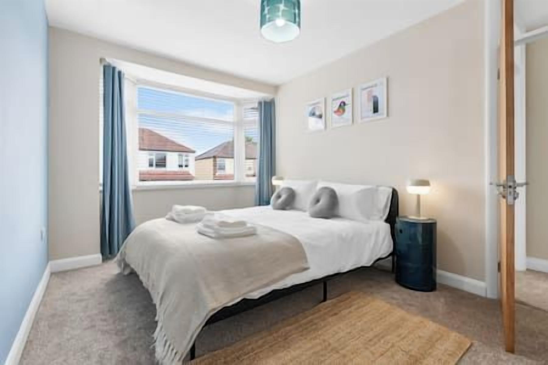 A bedroom with a bed, a bedside table, a lamp, a window with curtains, and a view of the outside.