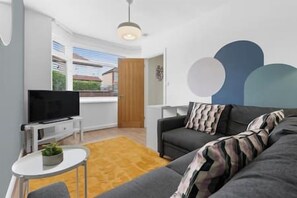 Ein modernes Wohnzimmer mit einer Couch, einem Fernseher und einem kleinen Tisch mit einer Pflanze.