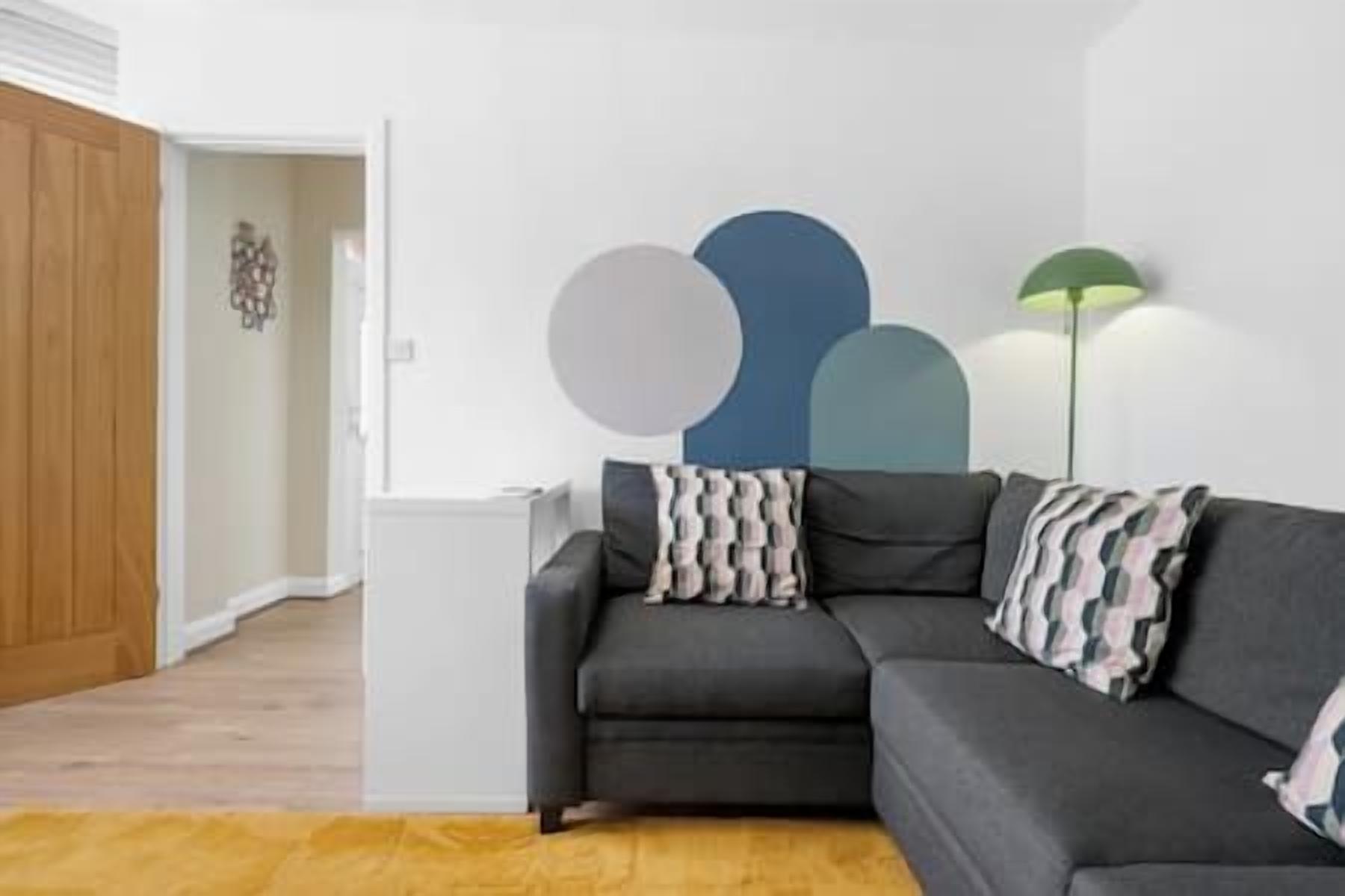 Un salon avec un canapé gris, un tapis jaune et un mur orné d’œuvres d’art abstraites.