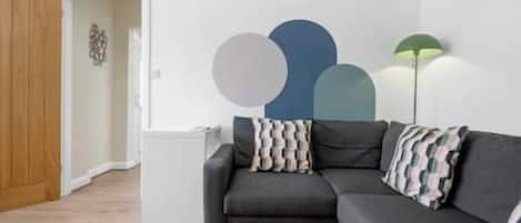 A living room with a grey sofa, a yellow rug, and a wall with abstract art.