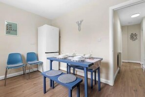 A room with a dining table, two chairs, a white cabinet, and a door leading to another room.