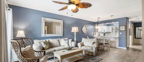 A living room with a ceiling fan, a sofa set, a coffee table, and a dining area with chairs.