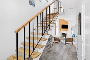 A staircase with wooden steps and black railings, leading to a room with a fireplace and a dining area with wicker chairs.