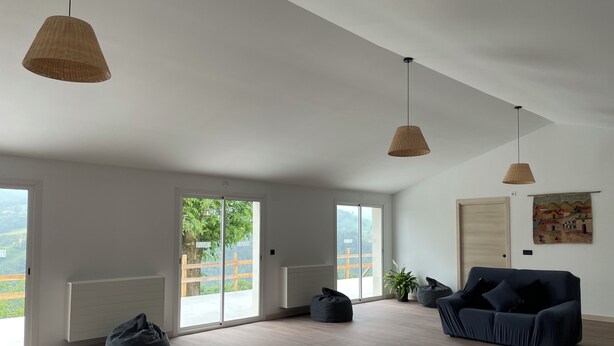 A spacious room with a high ceiling, large windows, and a sliding glass door leading to a balcony. There is a dark-colored sofa and a bean bag chair. - Larraitz Aterpetxea (PV)