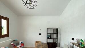 A modern, well-lit room with a wooden dining table, two colorful chairs, a bookshelf, and a hanging light fixture. - Larraitz Aterpetxea (PV)
