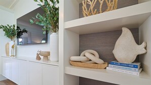 Un salón moderno con una consola blanca, un espejo grande y un estante con objetos decorativos y libros.