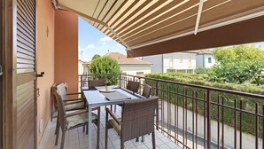 En balkon med bord og stole, en pergola over hovedet, og udsigt til omkringliggende bygninger og grønt.