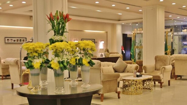 Eine geräumige Lobby mit einem runden Tisch, mehreren Sofas und einer großen Vase mit gelben Blumen.